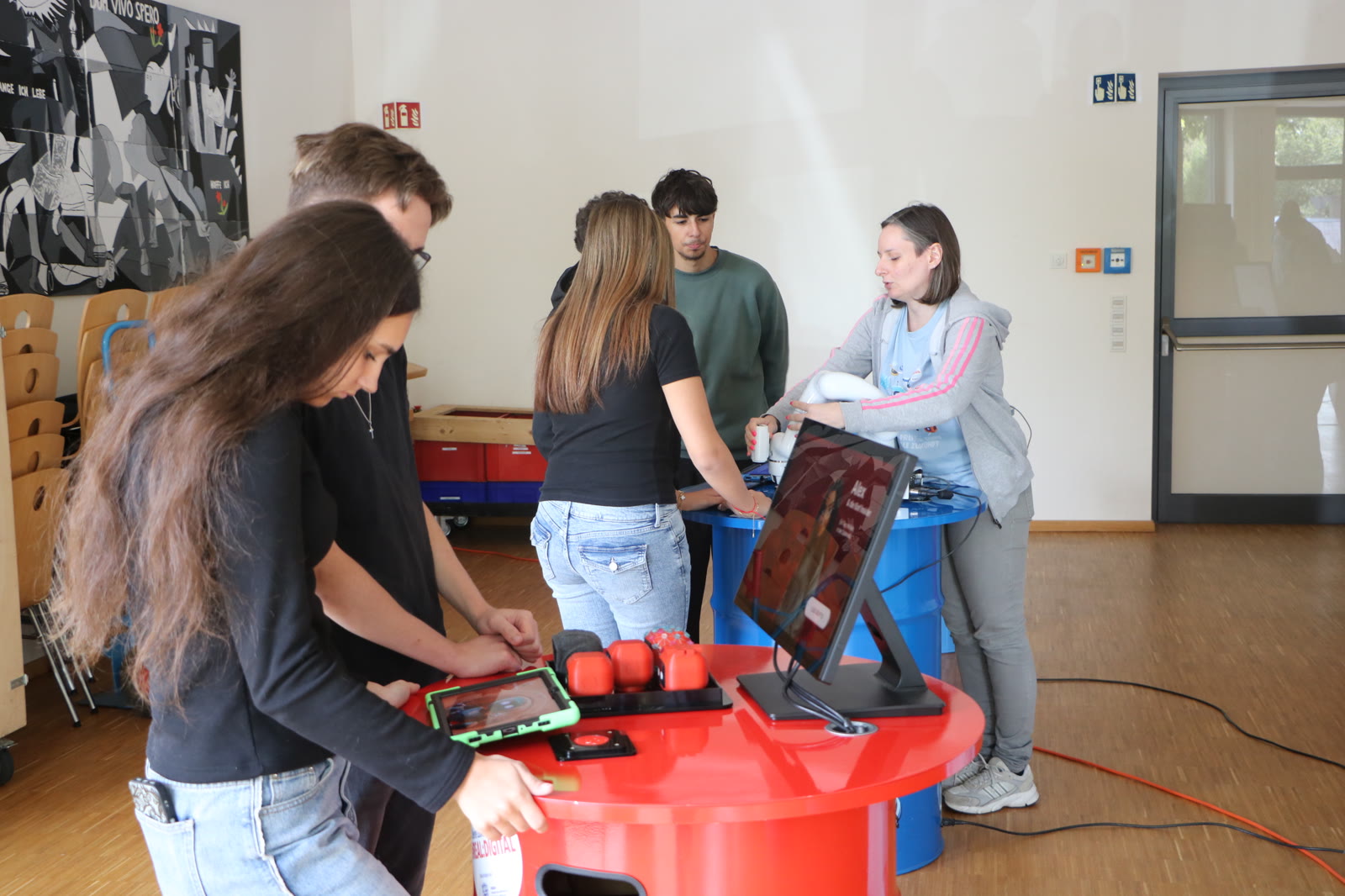 Teilnehmende arbeiten an digitalen Lernstationen mit Tablets und einem Roboterarm in der Aula der WKS Weilburg.