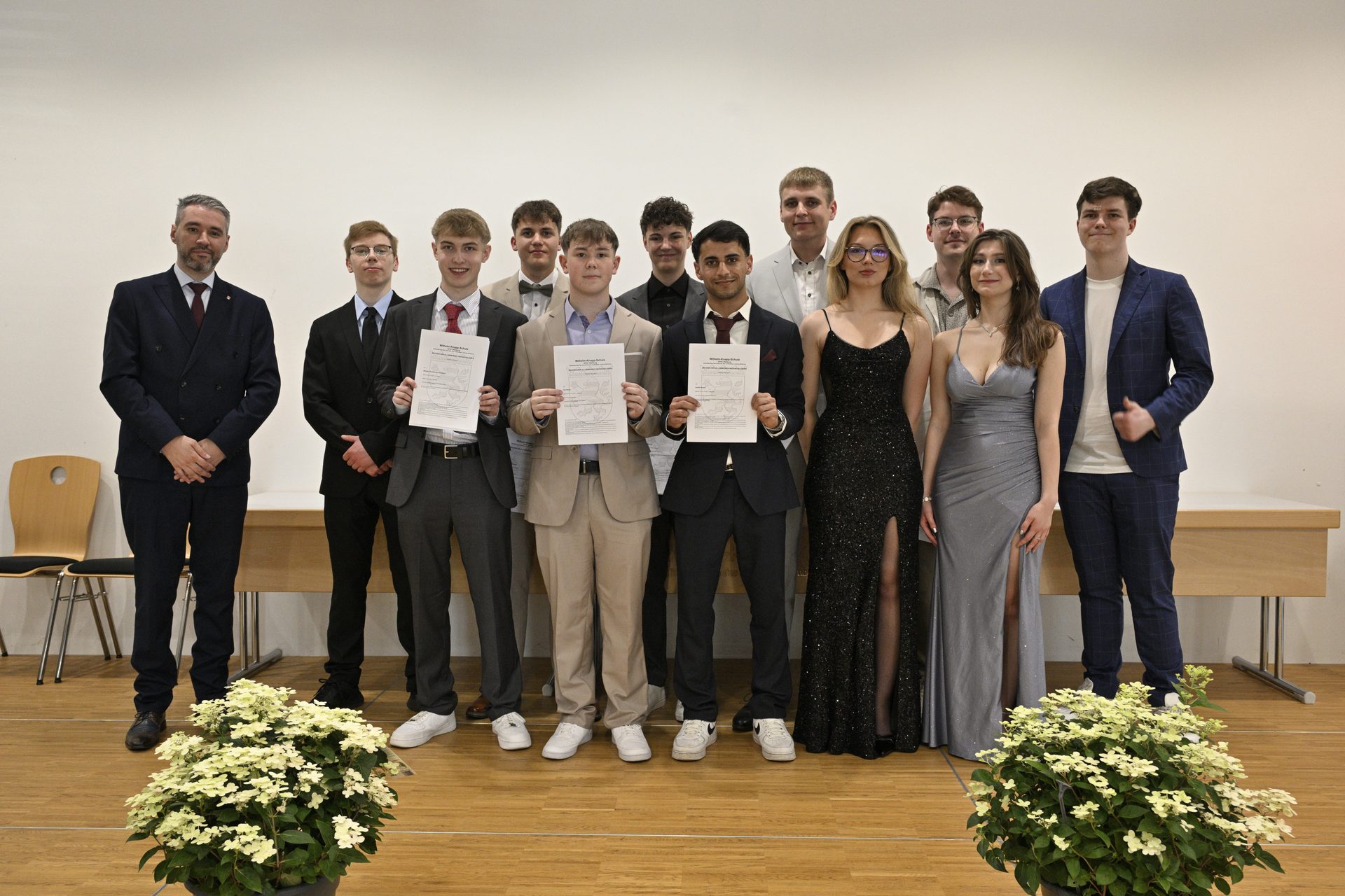 Abiturientinnen und Abiturienten einer Abschlussklasse des Beruflichen Gymnasiums mit ihrem Tutor bei der Zeugnisübergabe in der Aula der Wilhelm-Knapp-Schule Weilburg 2026