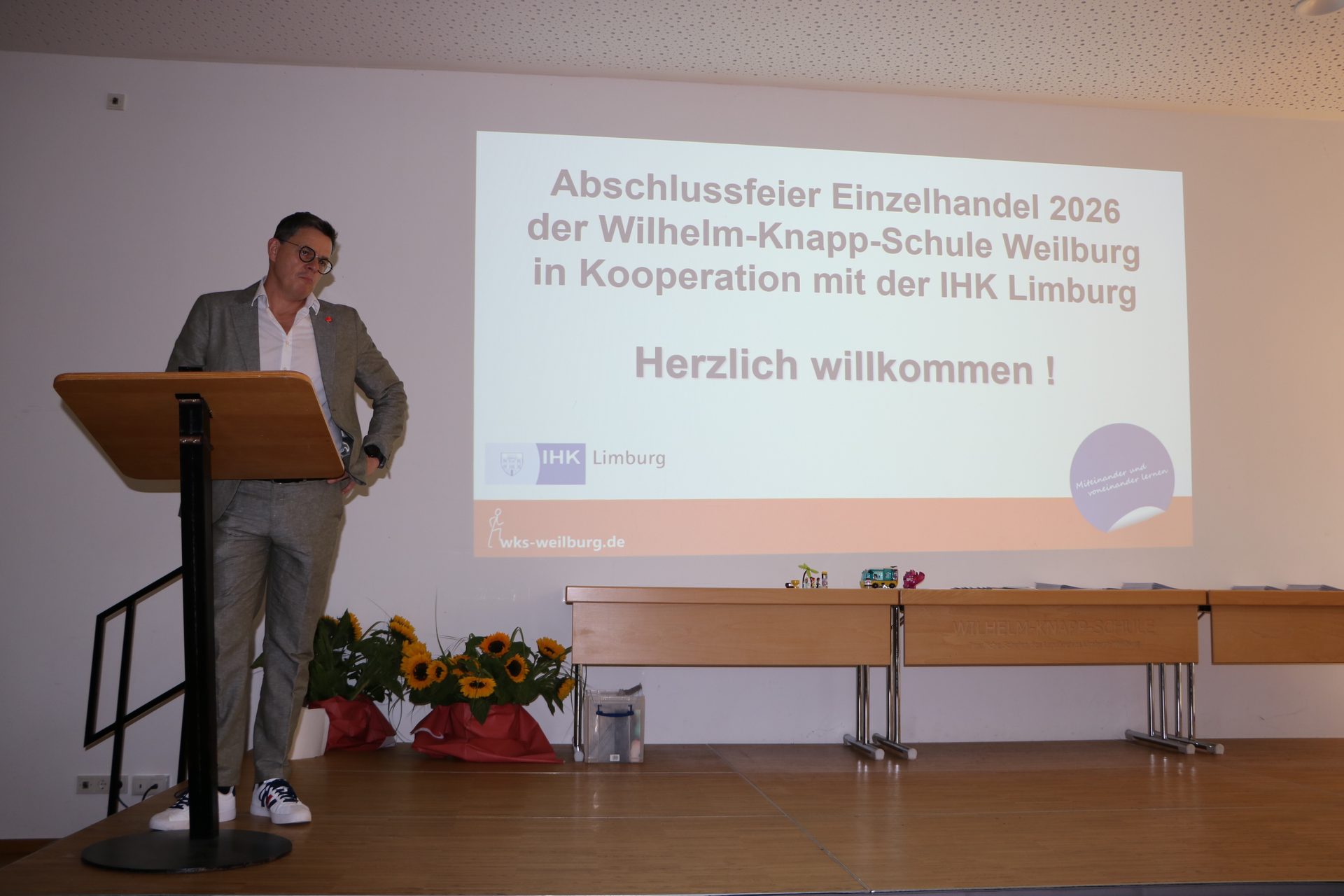Schulleiter Stefan Jeanneaux-Schlapp eröffnet die Abschlussfeier Einzelhandel 2026 der Wilhelm-Knapp-Schule Weilburg in Kooperation mit der IHK Limburg am Rednerpult in der Aula