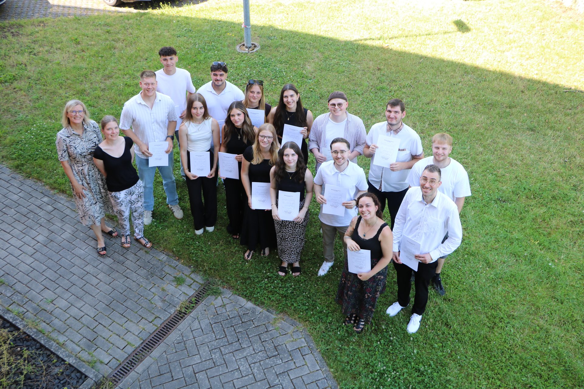 Die Absolventinnen und Absolventen der Klasse 12 XVF aus der Vogelperspektive mit ihren Abschlusszeugnissen auf der Wiese an der Wilhelm-Knapp-Schule Weilburg 2026